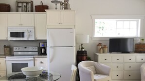 A compact kitchen with white cabinetry, a microwave, an oven, and a refrigerator. There is a glass table with a bowl, a chair, and a television on a stand. - One bedroom fully equipped Mahone Bay luxury cottage (Mahone Bay)