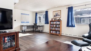 Ein Wohnzimmer mit Flachbildfernseher, einer Holzregal, einem Schreibtisch mit Stuhl und einer Ledersofa.