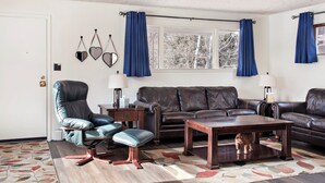 Ein Wohnzimmer mit einer braunen Ledersofa, einem blauen Ledersessel, einem Holztisch und einem Teppich mit Muster.