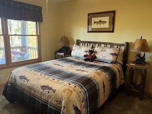 A bedroom with a large bed, a framed fish picture on the wall, and a window with a view of trees.