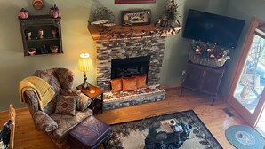 Ein gemütliches Wohnzimmer mit Kamin aus Stein, einer bequemen Couch, einem Couchtisch und einem an der Wand befestigten Fernseher.
