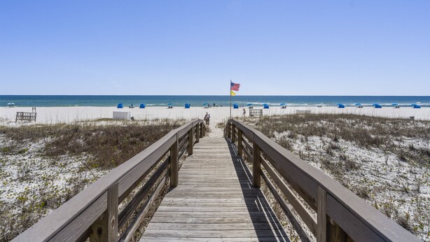 A wooden boardwalk leading to a beach with a flag. - Shipwatch 102A by Liquid Life (Pensacola)