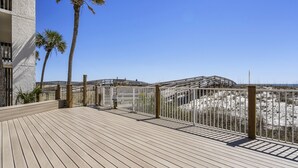 A wooden deck with a railing, overlooking a beach with palm trees and a clear sky. - Shipwatch 102A by Liquid Life (Pensacola)