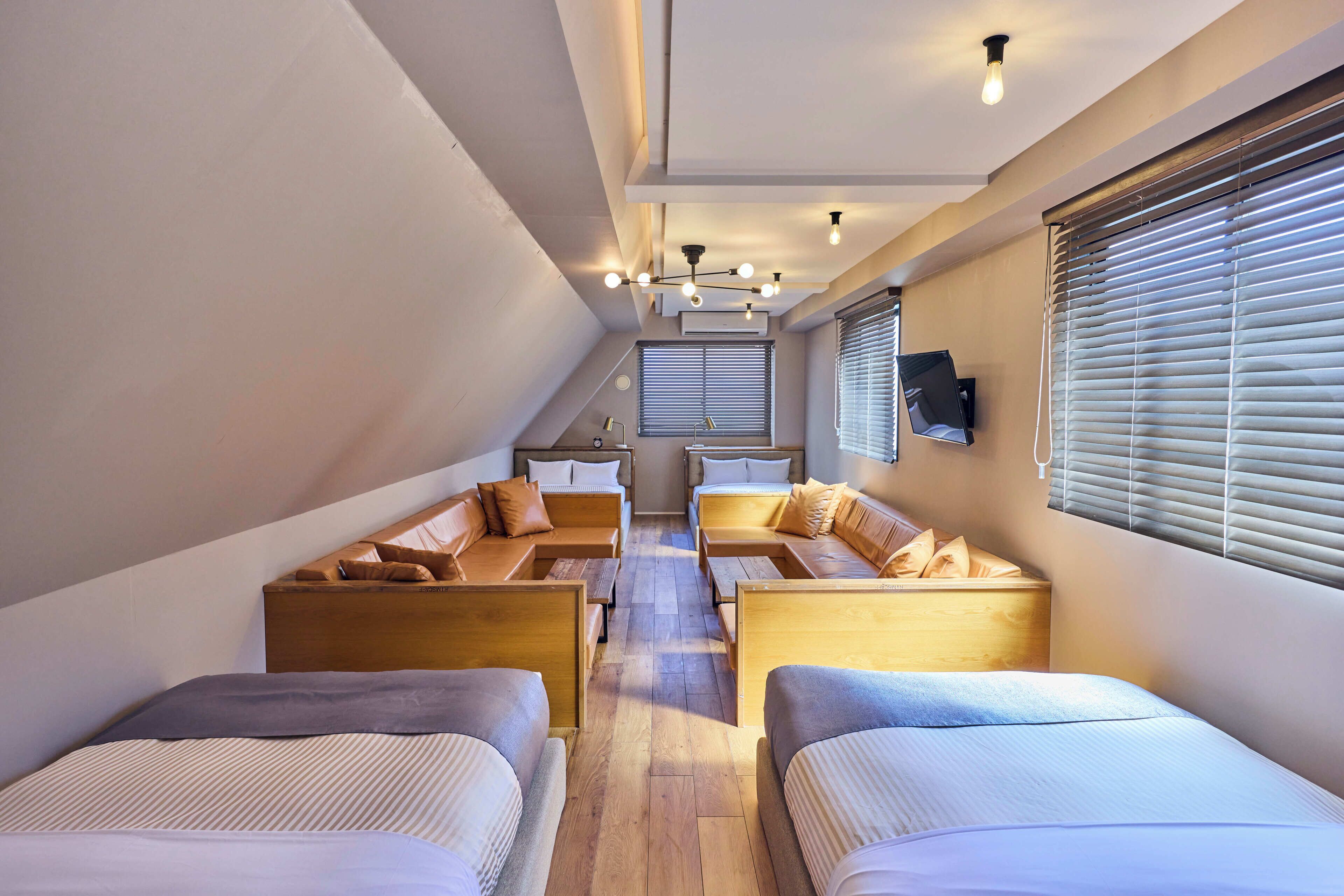 A modern hotel room with two beds, a sofa, and a small dining table.