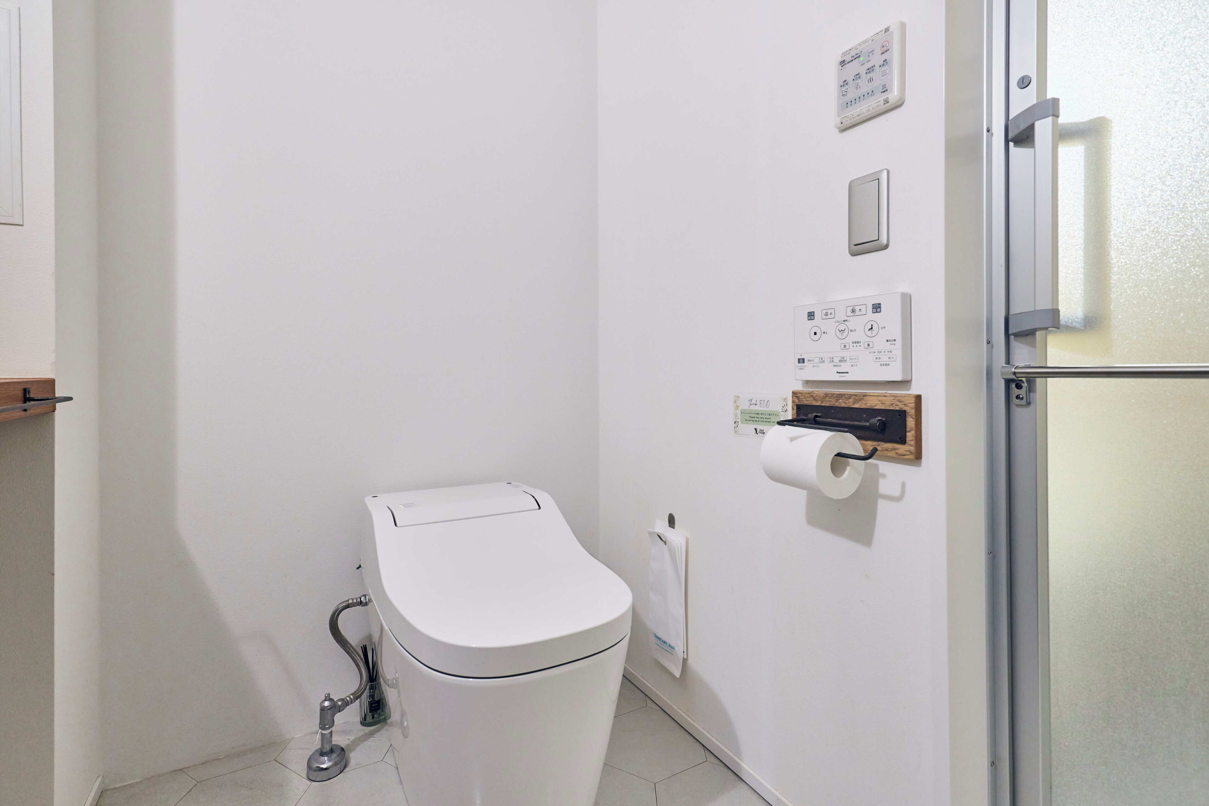 Een kleine, schone badkamer met toilet, een papieren handdoekdispenser en een handdroger aan de muur.