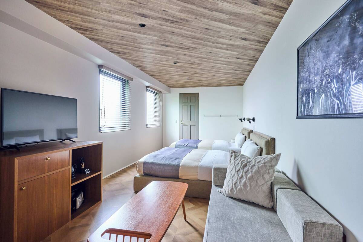 Een moderne slaapkamer met een houten plafond, een groot bed, een televisie, een houten kast en een bankje.