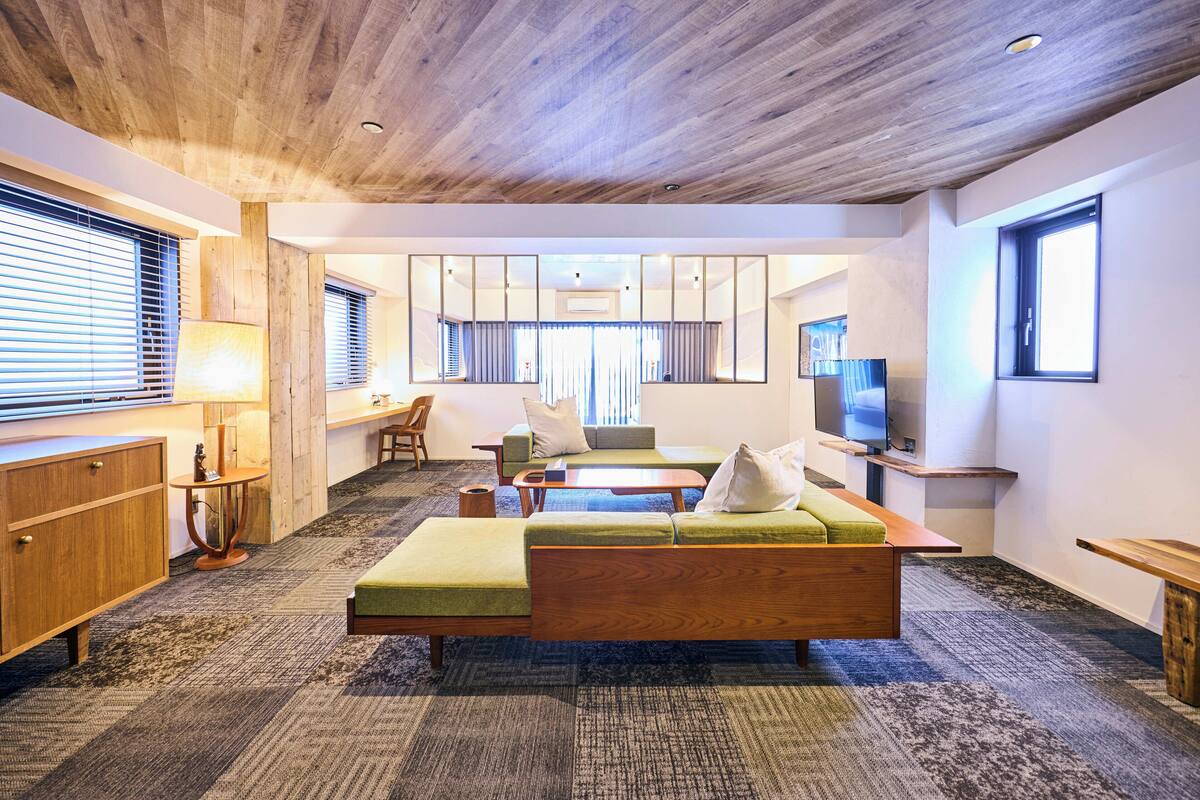 Een moderne woonkamer met een houten plafond, een groene bank, een houten salontafel en een televisie op een standaard.