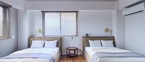 A room with two beds, a small table, and an air conditioning unit.