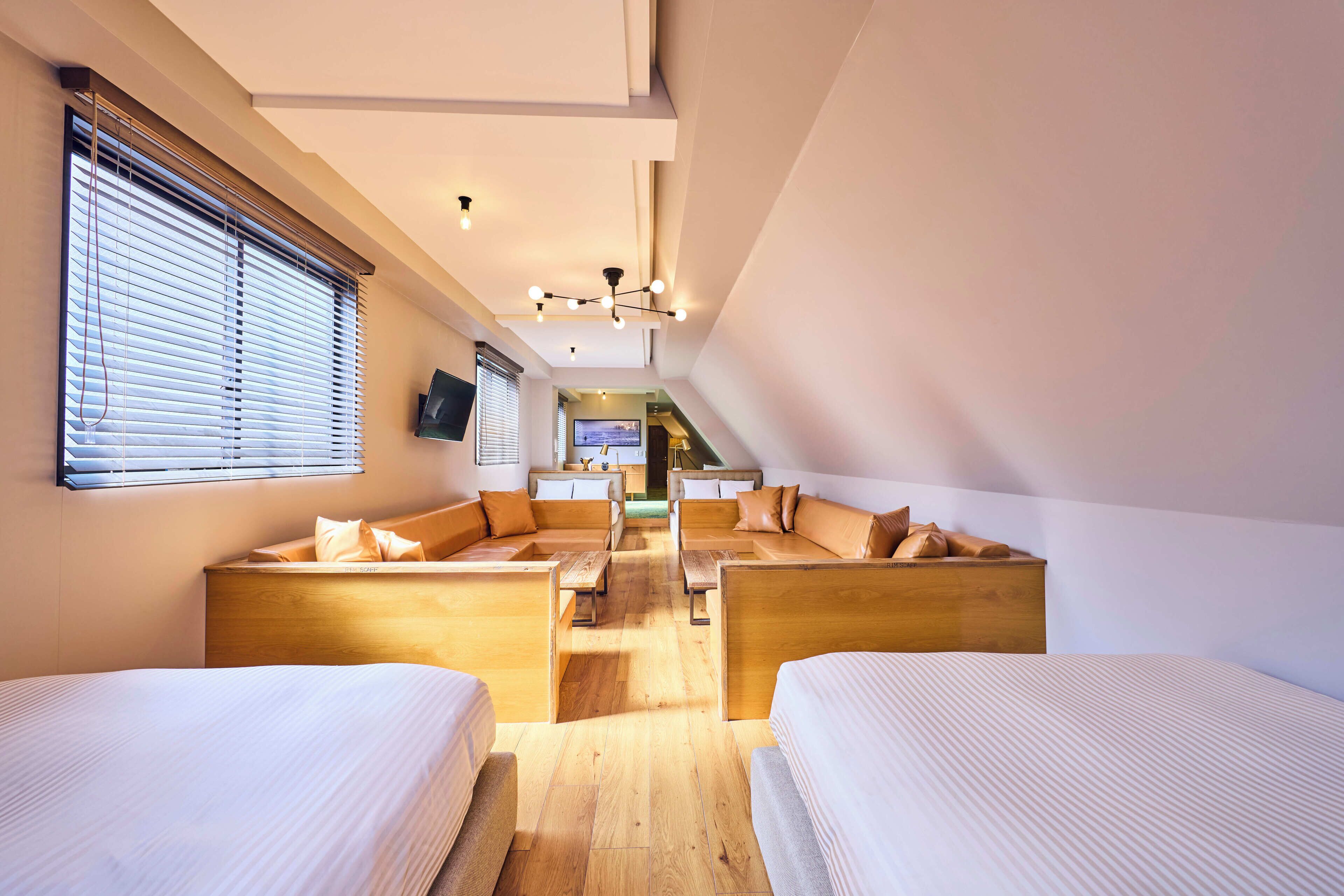 A modern hotel room with two beds, a sofa, and a TV.