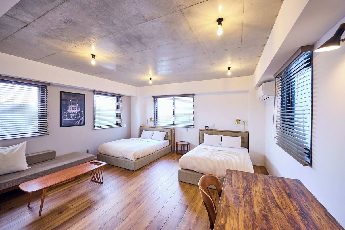 Een moderne slaapkamer met twee bedden, een houten bankje en een eettafel.