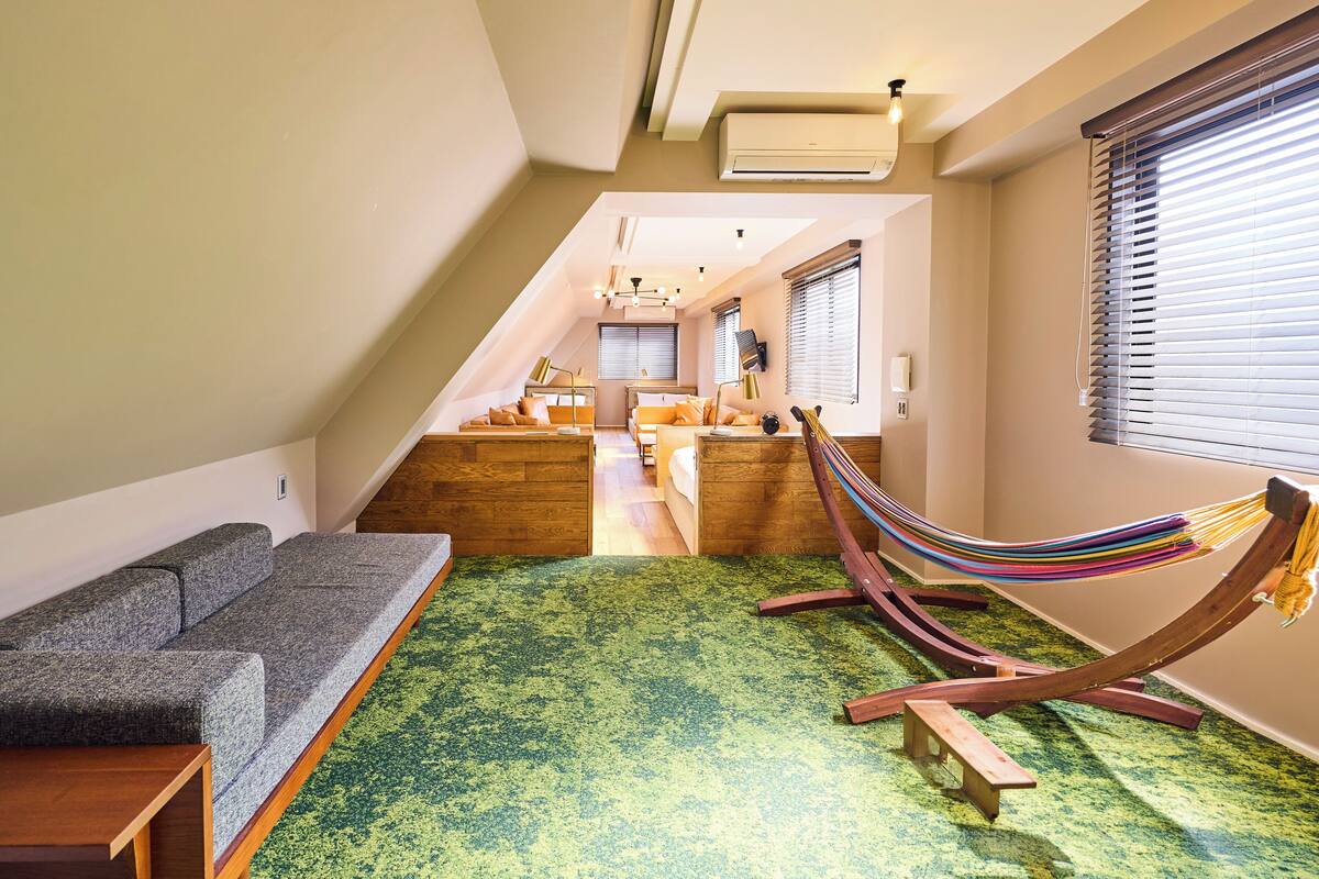 Een moderne loft slaapkamer met een groen tapijt, houten hoofdbord en een hangmat.