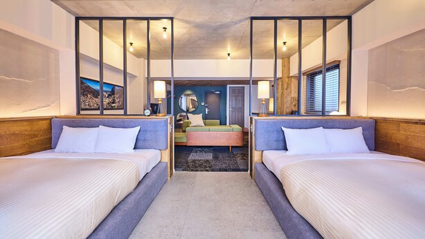 A hotel room with two beds, a central seating area, and a view of a mountain landscape through a large window.