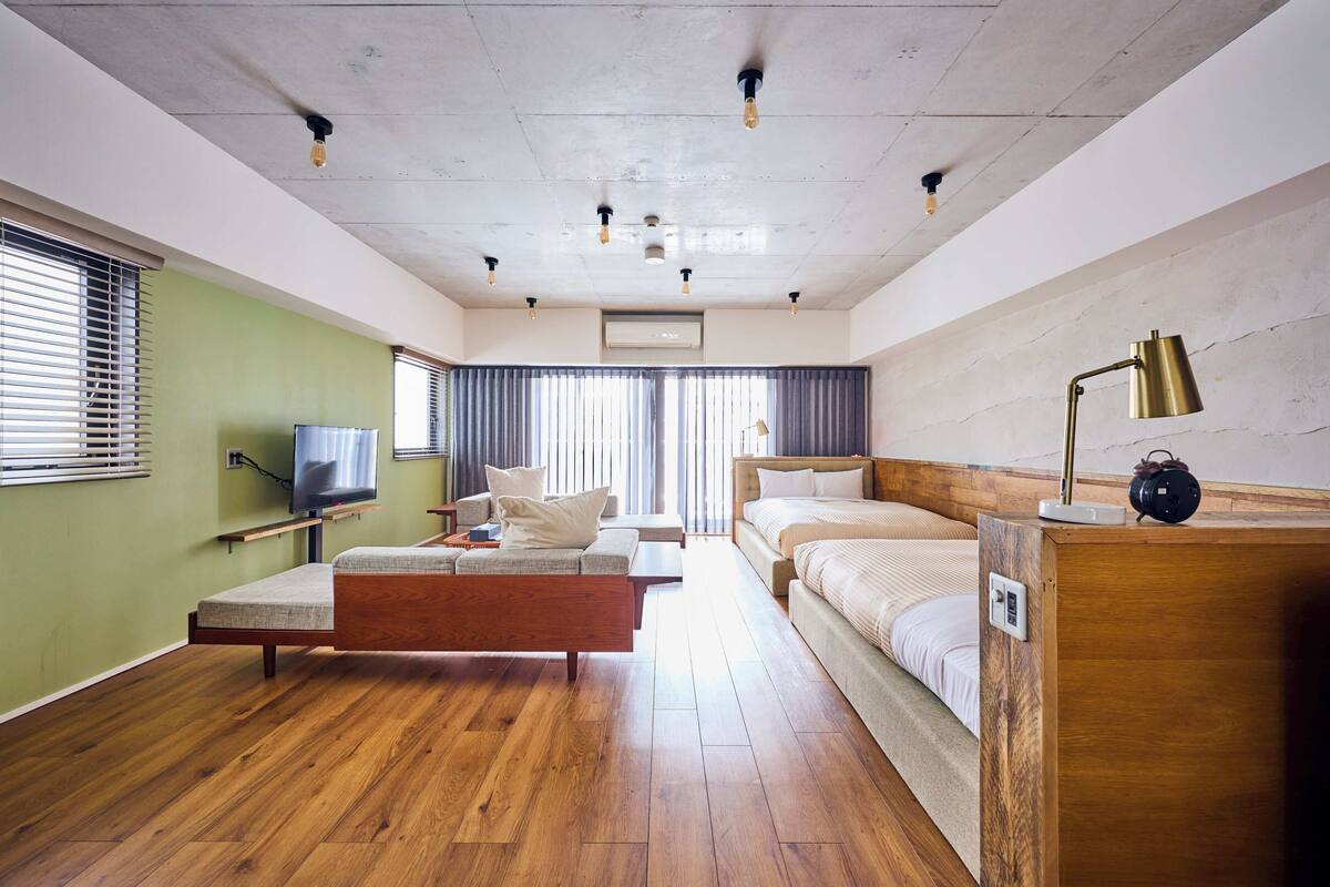 Een hotelkamer met een houten vloer, een bed, een bank, een televisie en een lamp.
