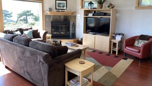 A living room with a fireplace, a television, a sofa, and a red armchair. - The Waves House! Breathtaking Ocean View, Hot Tub, King Beds, Dog-Friendly. (Waldport)