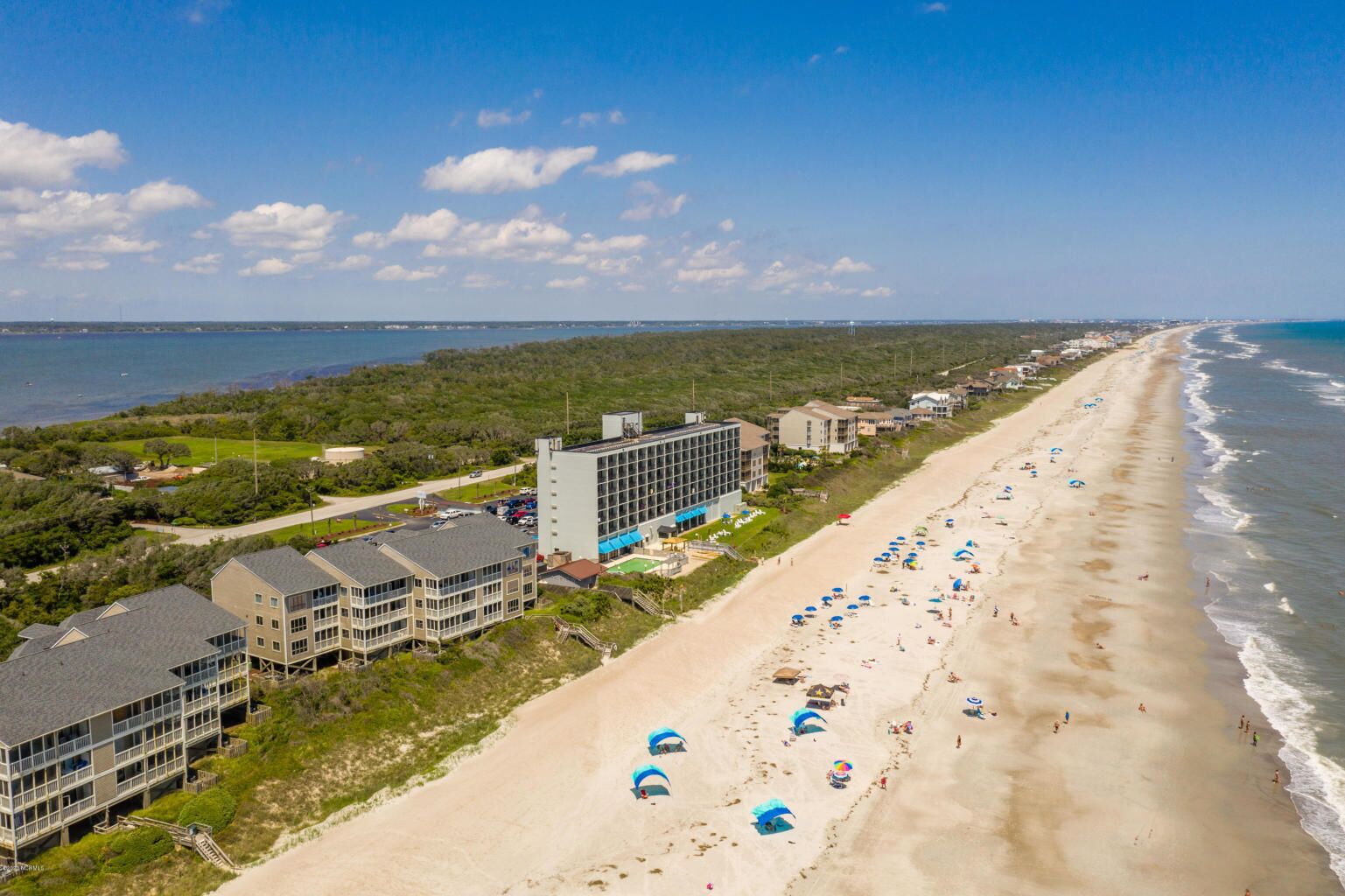 A coastal hotel with multiple buildings, a beach with umbrellas, and a view of the ocean.