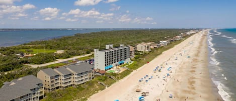 A coastal hotel with multiple buildings, a beach with umbrellas, and a view of the ocean.