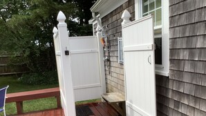 A wooden deck with a white gate leading to a house with a window. - Cape Cod Beach Cottage, only 5 minute walk to Glendon beach & local restaurants (Dennis)