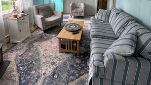 A living room with a patterned rug, a striped sofa, a patterned armchair, a wooden coffee table, and a ceiling fan. - Cape Cod Beach Cottage, only 5 minute walk to Glendon beach & local restaurants (Dennis)