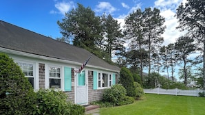 A house with a white picket fence, a well-maintained lawn, and a clear blue sky. - Cape Cod Beach Cottage, only 5 minute walk to Glendon beach & local restaurants (Dennis)