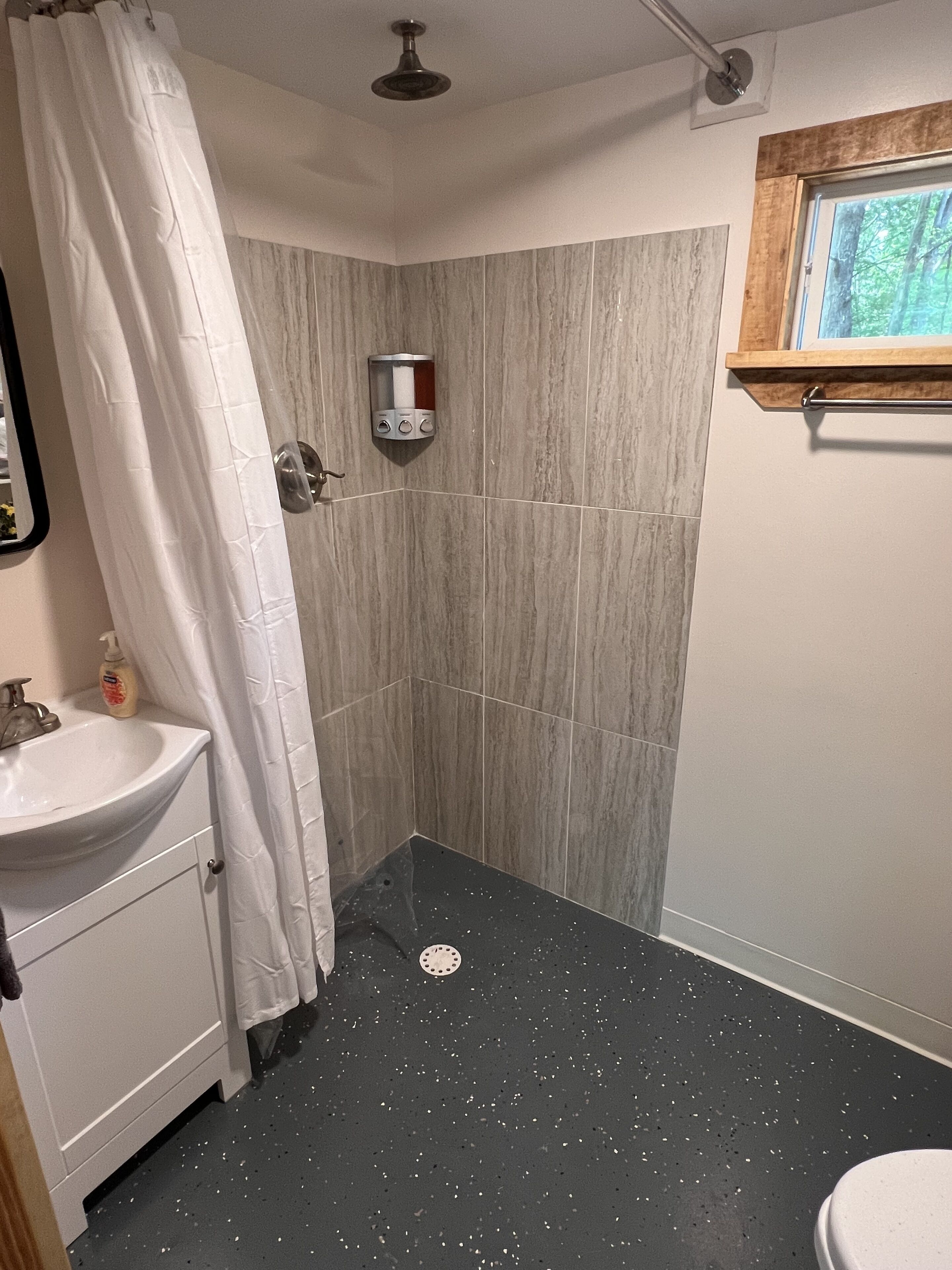A bathroom with a shower, a sink, and a window.