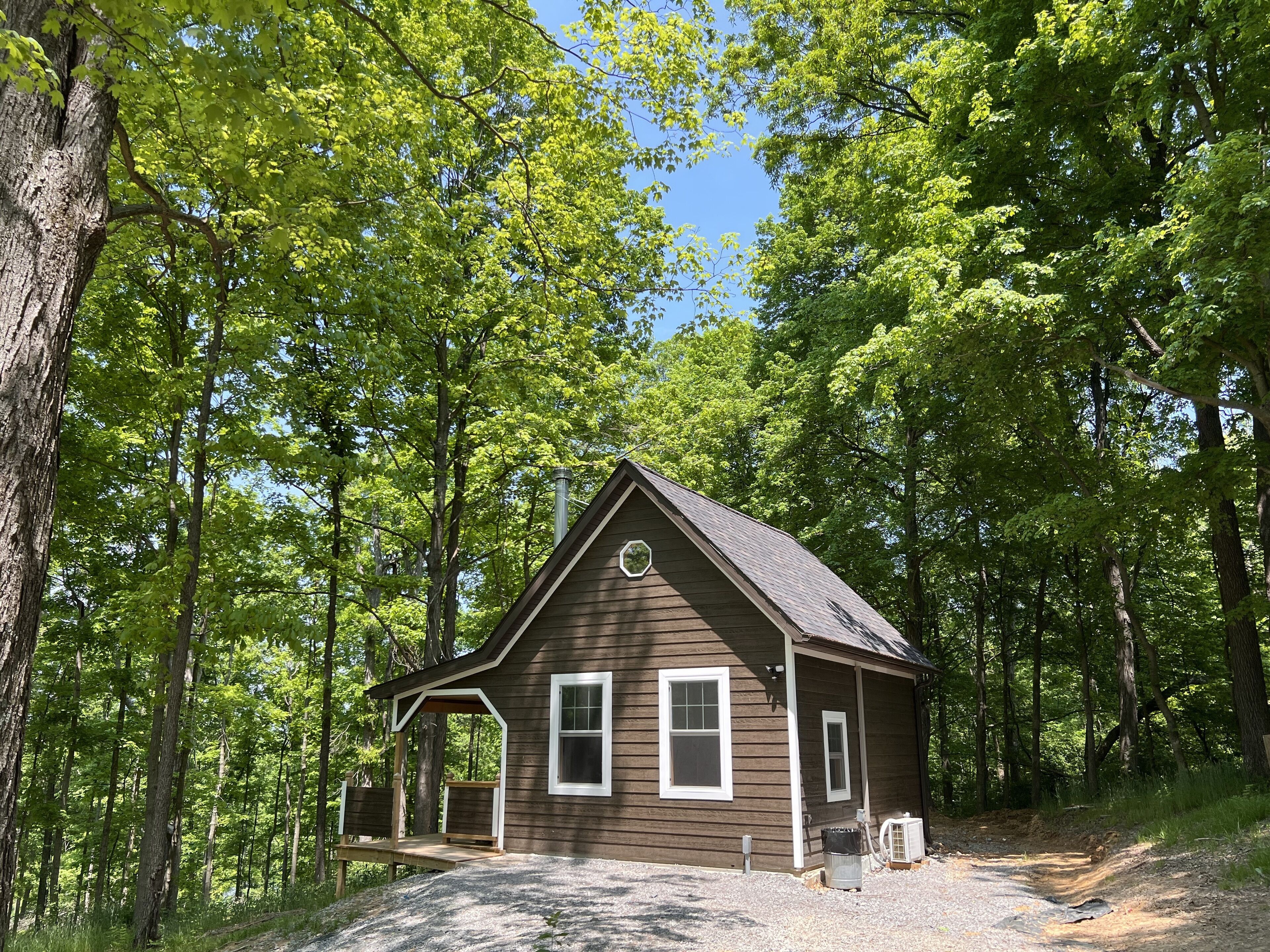 A small cabin with a porch, surrounded by tall trees.