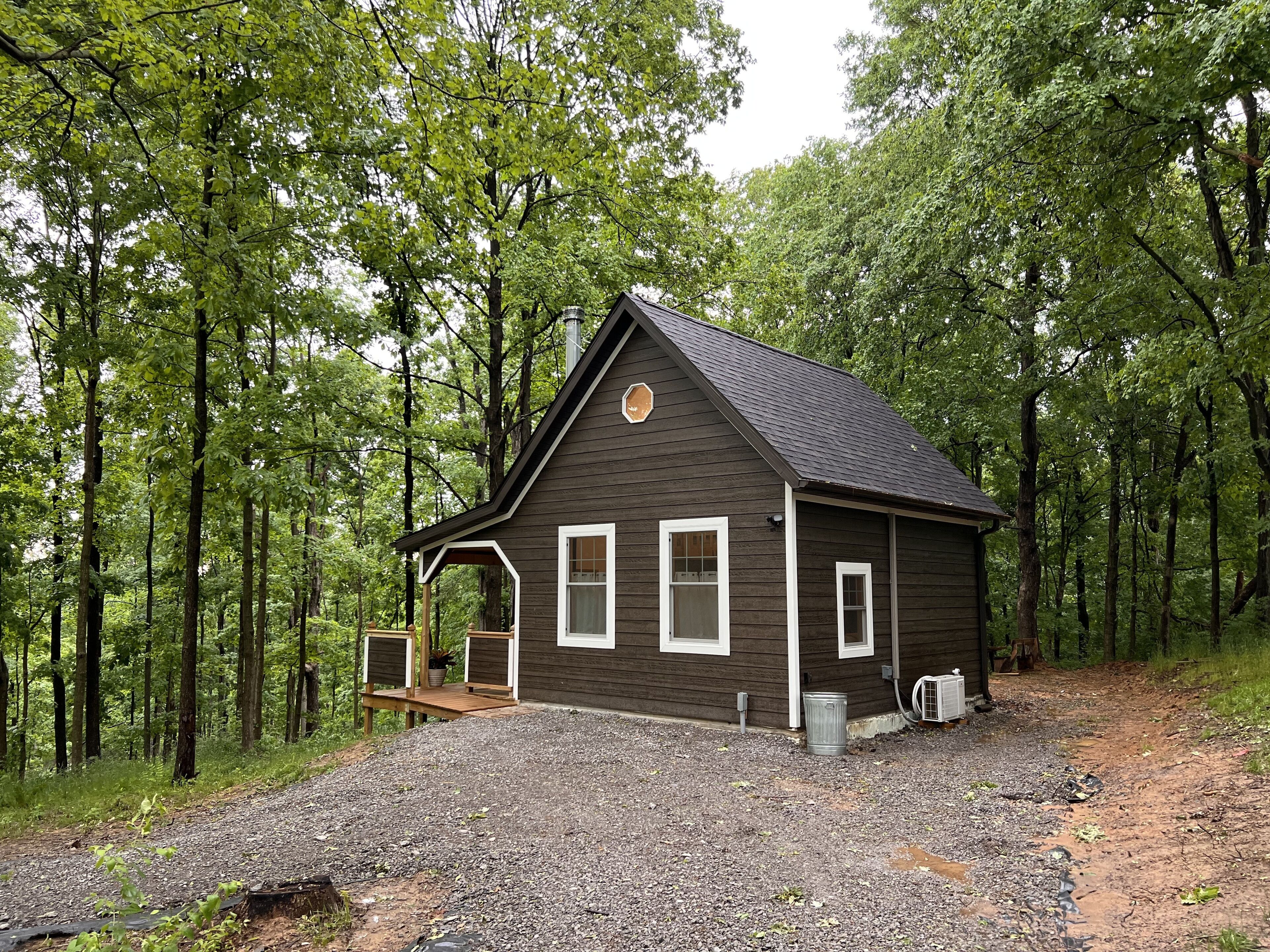 A rustic cabin with a sloped roof, surrounded by dense forest.