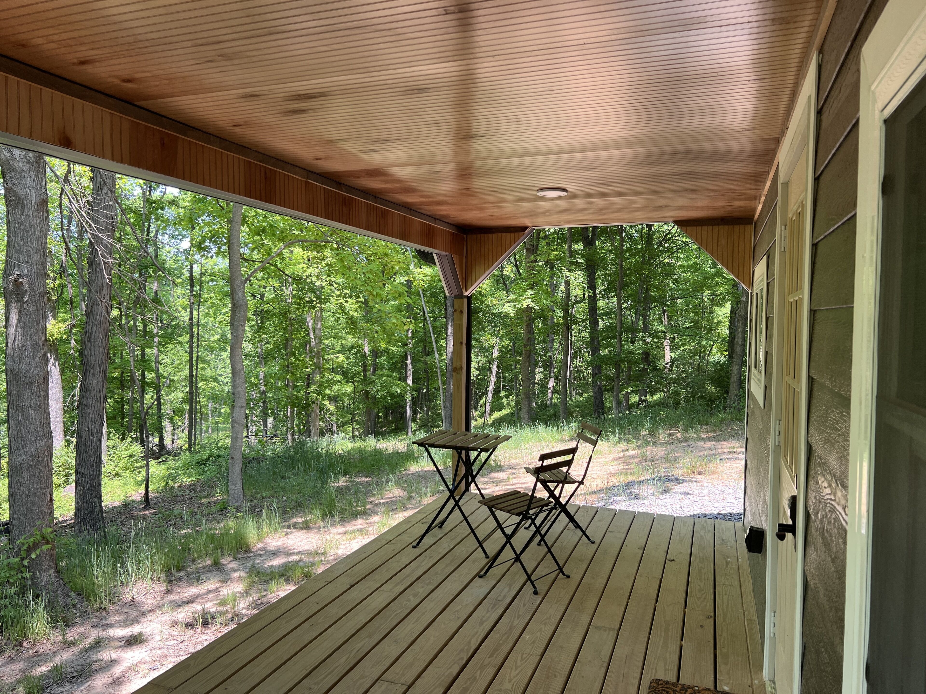 En overdækket veranda med et bord og stole, med udsigt over et skovområde.