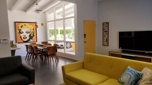 Ett modernt vardagsrum med en gul soffa, en matplats med trästolar, ett stort fönster och en platt-TV.