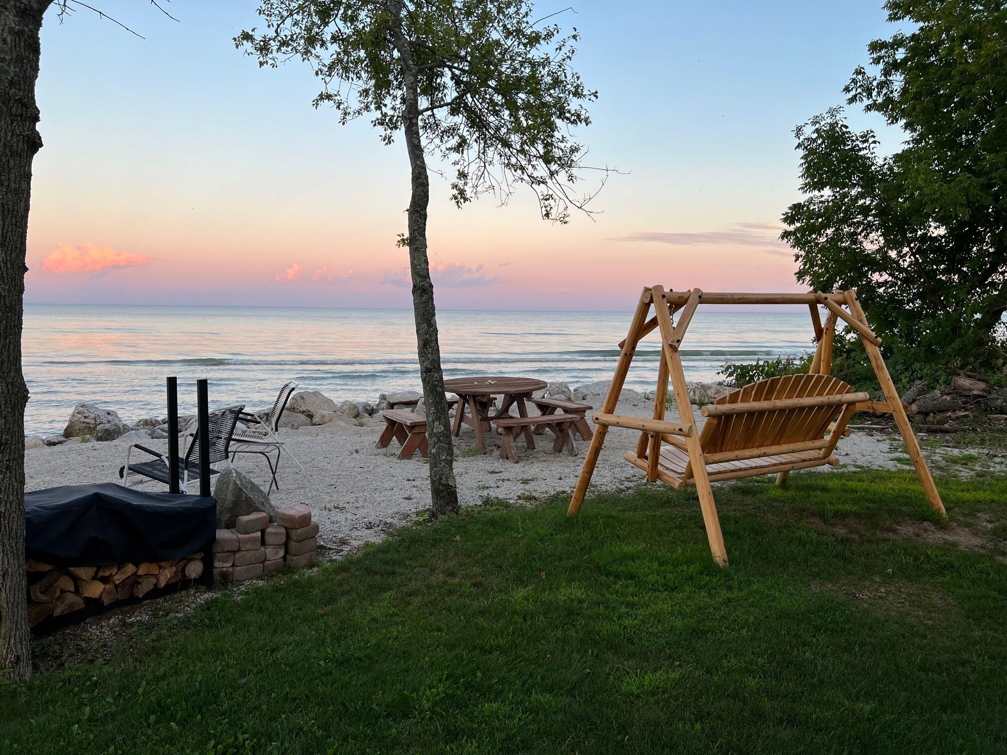 A beachside setting with a wooden swing, picnic tables, and a covered seating area.