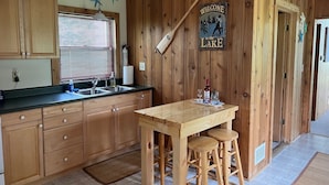 A wooden interior with a kitchen area featuring a wooden table, bar stools, and a welcome sign to the lake.