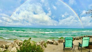 A beach with two turquoise beach chairs, a rocky shoreline, and a rainbow over the ocean.