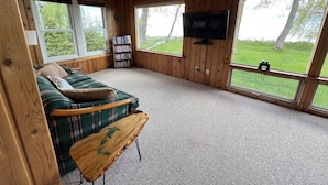 A cozy cabin interior with a sofa, a wooden coffee table, a bookshelf, and a TV mounted on the wall.