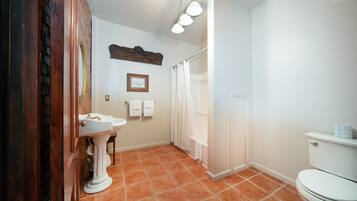 A bathroom with a pedestal sink, a toilet, a shower curtain, and a wall-mounted light fixture.
