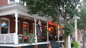 Ein Ziegelgebäude mit weißer Veranda, Sitzgelegenheiten im Freien und einer Flagge.