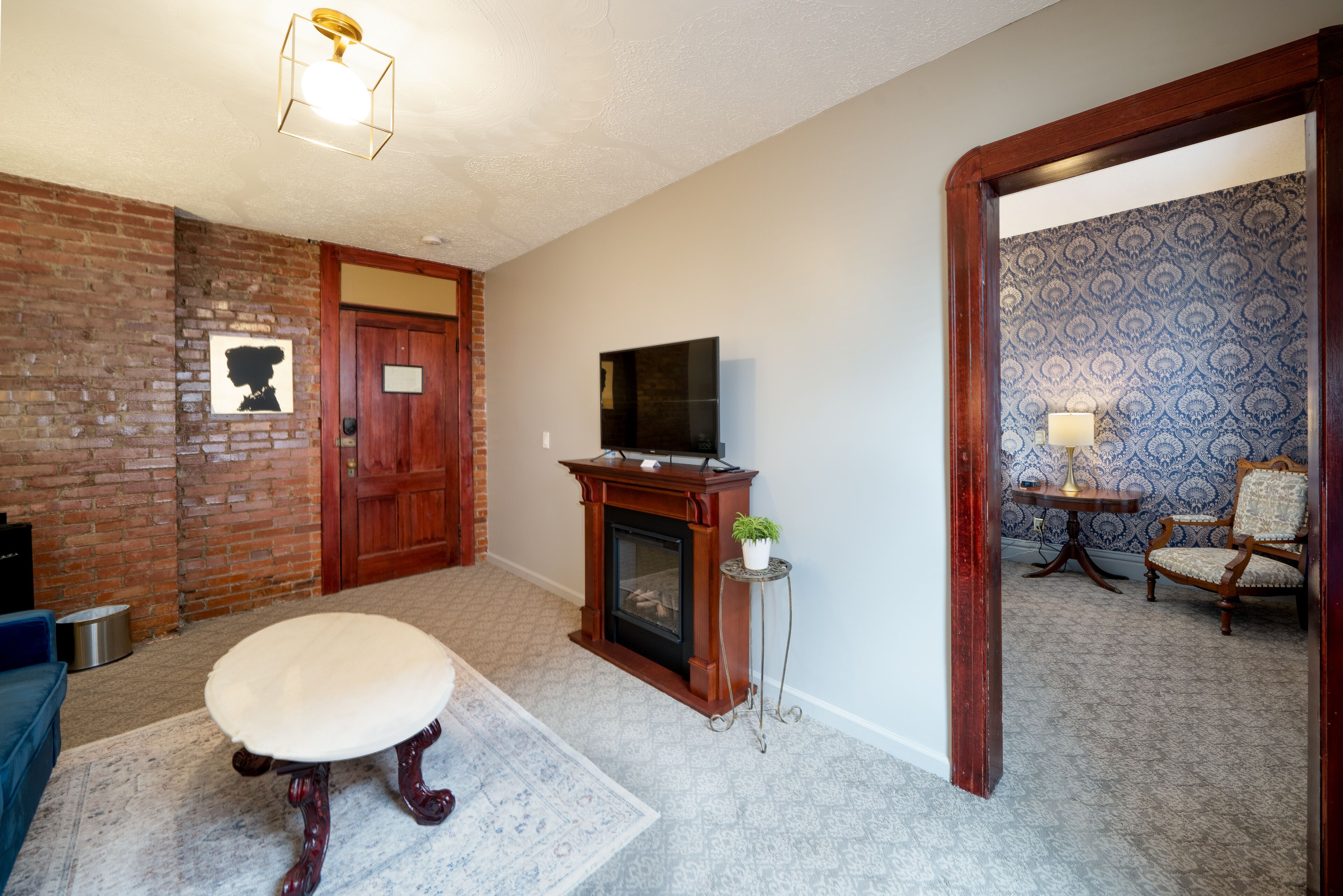 A living room with a fireplace, a television, a blue sofa, and a patterned wallpaper wall.