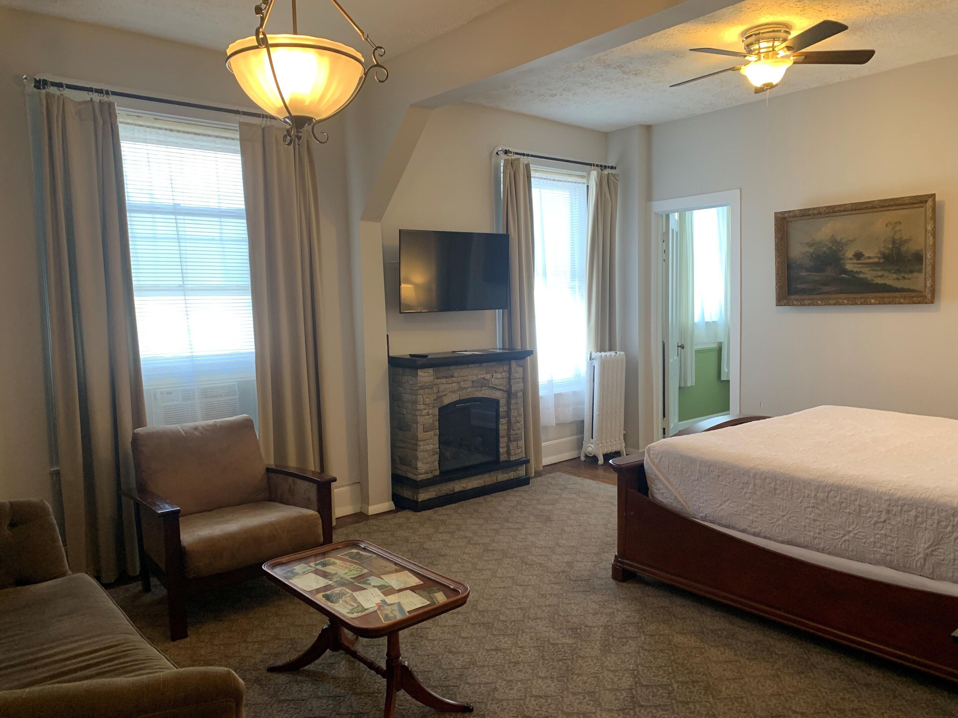 A hotel room with a bed, a chair, a table, a fireplace, a television, and a ceiling fan.