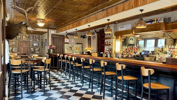 Eine Bar mit Schachbrettfußboden, einer Holztheke und mehreren Barhocker.