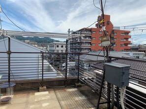 Terraço com grades de metal, uma mesa e um quadro de eletricidade.