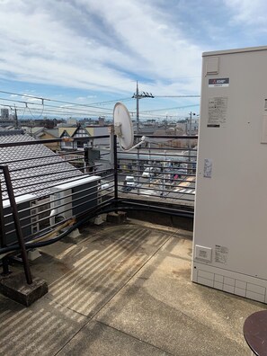 Terraço com antenas parabólicas, uma caixa elétrica branca e vista para a paisagem urbana.