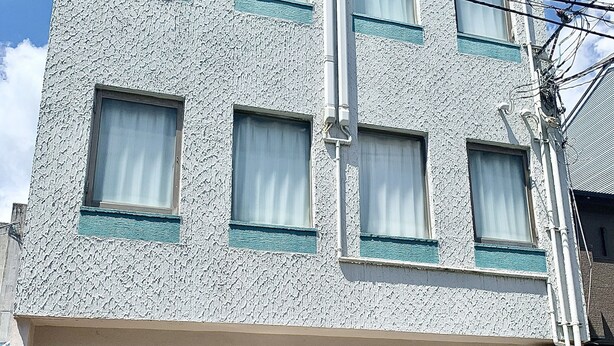 Un edificio de varios pisos con fachada texturizada, una bicicleta estacionada en la entrada y un cielo despejado.