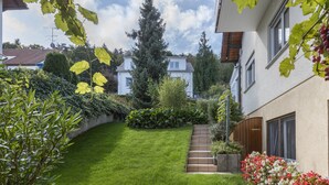 Un jardín cuidado con césped, un sendero de madera y diversas plantas y arbustos.