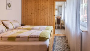 Un dormitorio con dos camas, paredes de paneles de madera, una ventana con cortinas y vista a otra habitación.