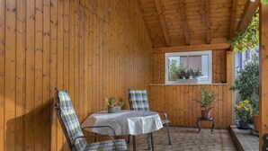 Una habitación con paneles de madera, una mesa y sillas, un ventanal con plantas y piso de baldosas.