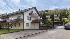 Un edificio residencial de dos plantas con garaje, entrada para vehículos y un automóvil estacionado.