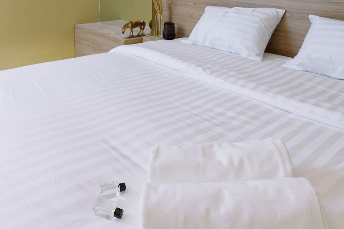 A neatly made bed with white linens, a wooden headboard, and a bedside table with a small decorative item.