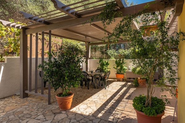 A covered patio area with stone flooring, potted plants, and outdoor furniture.