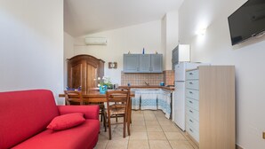 Un espacio habitable pequeño con un sofá rojo, una mesa de comedor de madera, una zona de cocina con armarios y un televisor montado en la pared.