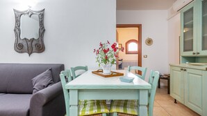 Zona pranzo con tavolo, sedie, un vaso con fiori, un divano e angolo cottura con pensili.