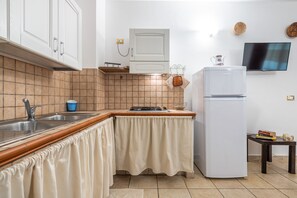 Une cuisine équipée d’un évier, d’une cuisinière et d’un réfrigérateur, avec un dosseret carrelé et des meubles blancs.