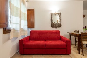 Un canapé rouge, un meuble en bois, un miroir, une table à manger avec des chaises et une fenêtre avec des rideaux.